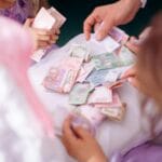 Dziecko i dorosły liczą kolorowe banknoty na stole podczas nauki oszczędzania