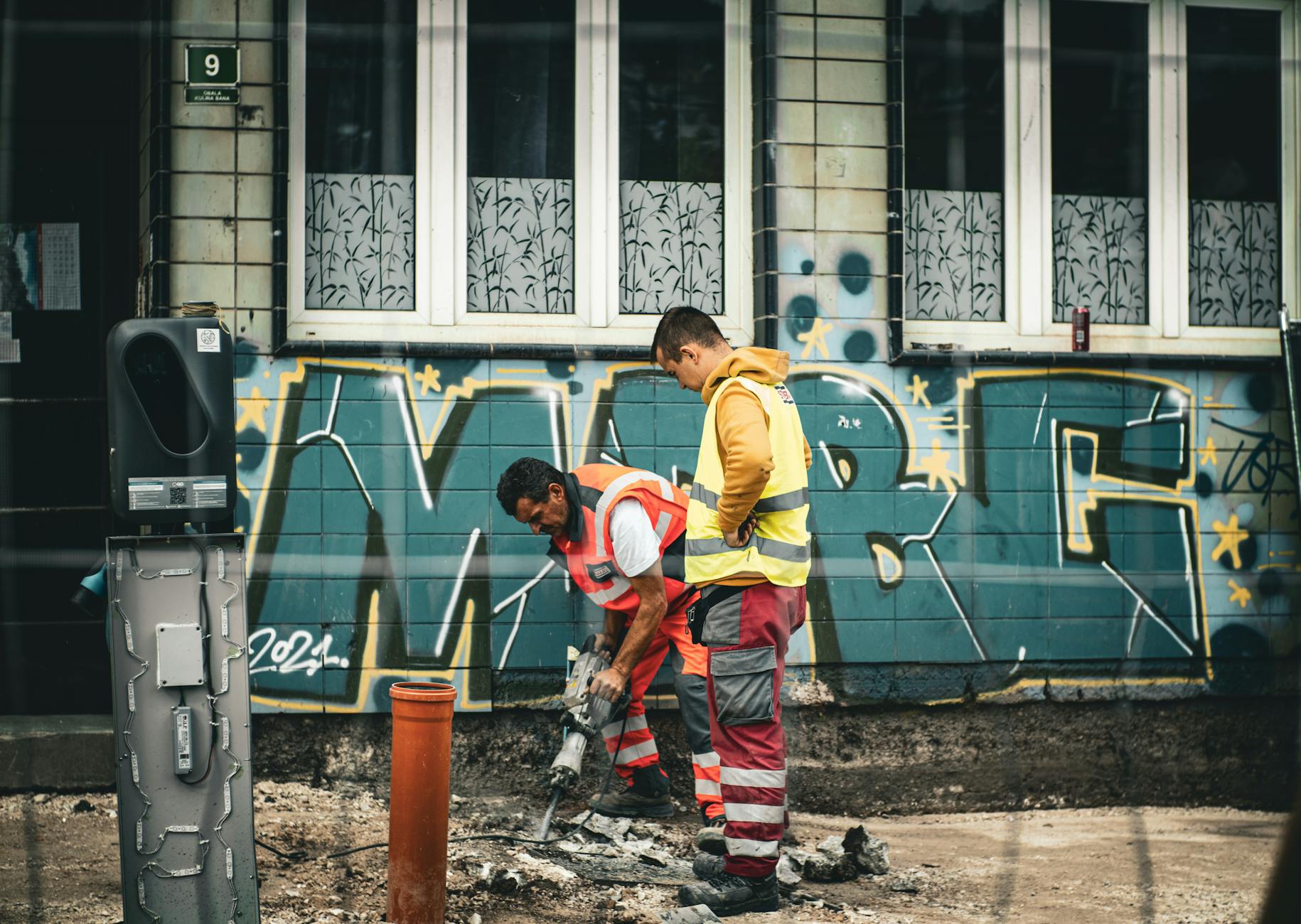 Robotnicy drogowi przy naprawie ulicy na tle graffiti w Sarajewie