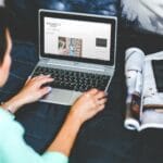 Kobieta leżąca w łóżku bloguje na laptopie z magazynem obok