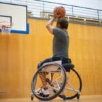 Mężczyzna na wózku inwalidzkim rzuca do kosza na hali sportowej